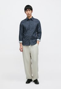 Καταδυτικό μπλε πουκάμισο με λουλουδάτο σχέδιο, με κουμπιά στο μπροστινό μέρος και γυρισμένα μανίκια, συνδυασμένο με ανοιχτόχρωμο λινό παντελόνι και μαύρα παπούτσια. Χαλαρή εφαρμογή και υφή υφάσματος.