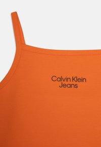 Pomarańczowy top na ramiączkach z cienkimi paskami, z czarnym logo "Calvin Klein Jeans" umieszczonym na środku przodu. Gładka, elastyczna tekstura materiału.