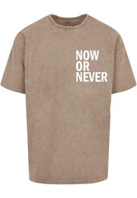 Brun bomulds t-shirt med afslappet pasform, rund hals og hvid tekst "NOW OR NEVER" på den øverste venstre side. Blød, falmet tekstur.