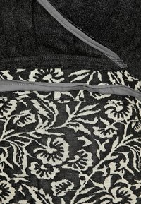 Svart tyg med ett blommönster i kräm, med en texturerad övre del och grå kant. Designen kombinerar släta och vävda texturer.