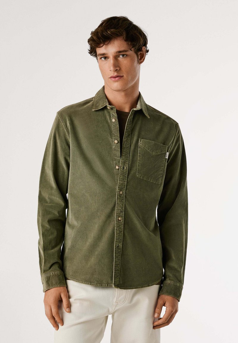 Camisa de pana verde oliva con cuello, cierre frontal con botones, un bolsillo en el pecho y botones en un acabado metálico claro.