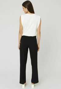 HAut en blanc sans manches associé à un pantalon noir taille haute ; tissu lisse avec une coupe décontractée ; modèle de dos face au spectateur.