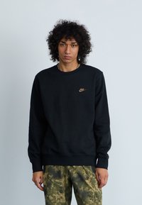 Čierna mikina vyrobená z bavlny, s okrúhlym výstrihom a rebrovanými manžetami. Malé, vyšívané logo Nike v bronzovej farbe na hrudi.
