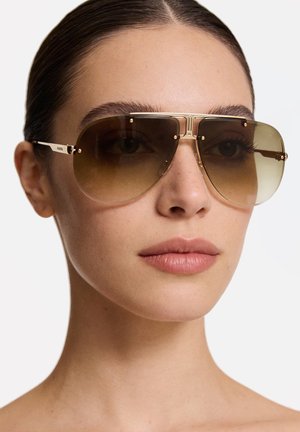 Occhiali da sole con montatura in metallo tono oro, lenti sfumate marroni e accenti prominenti sulla barra superiore; superficie liscia e riflettente; design oversize.