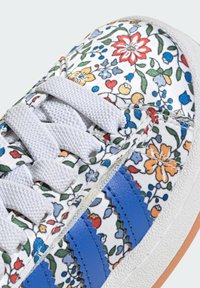 Floral-patterned sneaker with a white fabric upper, blue leather stripes, and white laces. Features a textured rubber sole.