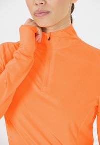 Langærmet atletisk trøje i skarp orange med en lynlåskrave og struktureret stof for åndbarhed og komfort.