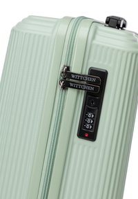 Hard-shell suitcase in light green, featuring a ribbed texture, double zippers, and a combination lock with a black accent.