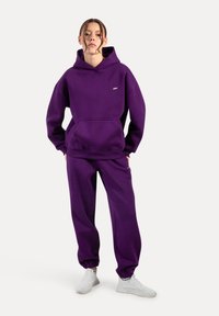 Lila Kapuzenpullover und passende Jogginghose aus weichem Stoff. Kapuzendesign mit Fronttasche, elastischen Bündchen und einem kleinen Logo-Detail.