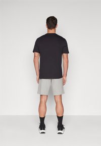 Camiseta de algodón negra de manga corta, combinada con pantalones cortos gris claro. El conjunto presenta un diseño simple, sin patrones, y zapatillas deportivas.