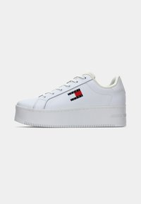 Weiße Plattform-Sneaker mit einem glatten Lederobermaterial, abgerundeter Spitze, flachen Schnürsenkeln und sichtbarer Gummisohle. Mit einem Logopatch in Rot, Weiß und Blau.