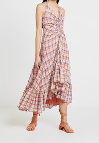 Halter-neck klänning med en vriden front, lager-på-lager fåll, färggård rutigt mönster och en flödande silhuett. Kombinerad med orange remsandaler.