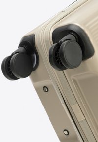 Hard-shell suitcase in light gold with a textured surface, featuring two black spinner wheels and a zipper closure.