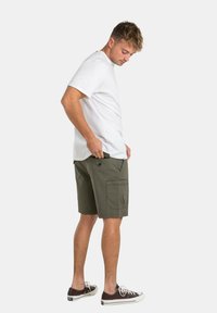 Pantalones cortos de cargo verde oliva con bolsillos laterales, fabricados en una mezcla de algodón, combinados con una clásica camiseta de manga corta blanca y zapatillas oscuras.