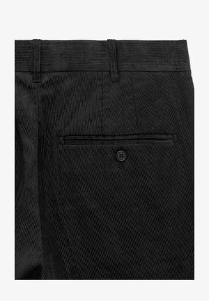 Tissu en velours côtelé noir avec nervures verticales, doté d'une poche arrière avec fermeture par bouton noir et d'une ceinture ajustée.