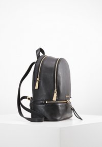 Sac à dos en cuir noir avec double zip, accessoires en doré, texture lisse, forme arrondie et sangle réglable. Comprend une poche zippée à l'avant.