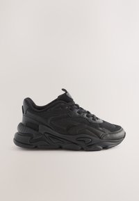 Baskets de sport noires avec une semelle épaisse et texturée, fermeture à lacets à l'avant et col rembourré, vues de côté sur un fond clair uni.