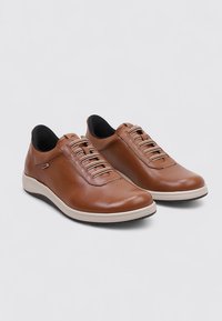 Zapatos de cuero marrón con un diseño elegante, punta redondeada, cordones elásticos y una suela de goma de color claro. Detalles texturizados cerca de los cordones.