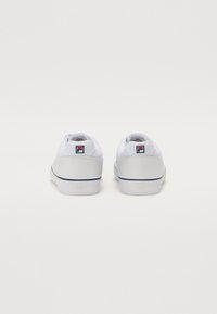White sneakers with a smooth leather heel, fabric upper, and visible branding on the back. Features a blue and red accent stripe.