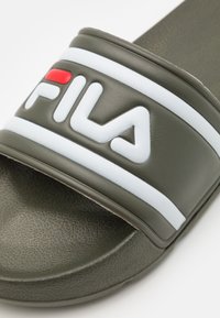 Chinelo de borracha verde com sola texturizada e uma tira larga exibindo o logo FILA em branco e vermelho, com detalhes em riscas.