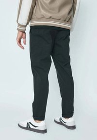 Pantalon noir fuselé en mélange de coton, comprenant des poches latérales. Assorti à des baskets blanches avec des rayures noires. Fond neutre.