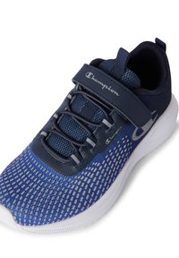 Zapatilla deportiva azul con parte superior de malla y suela de goma. Presenta una correa de velcro, cordones elásticos y un patrón texturizado en la zona de los dedos.