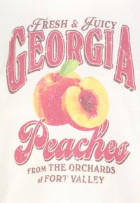 Weißer Stoff mit einem Design, das großen Text mit der Aufschrift "Georgia Peaches" zeigt, begleitet von einer ganzen Pfirsichfrucht und einem halbierten Pfirsich mit einem grünen Blatt.