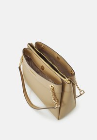 Sac à main beige avec accents en chaîne dorée, double compartiments, fermeture à glissière et texture lisse. Présente une seule longue poignée pour le transport.