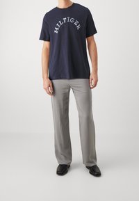 Camiseta de algodón navy con el texto "HILFIGER" en arco blanco, combinada con pantalones relajados gris claro y zapatos negros.