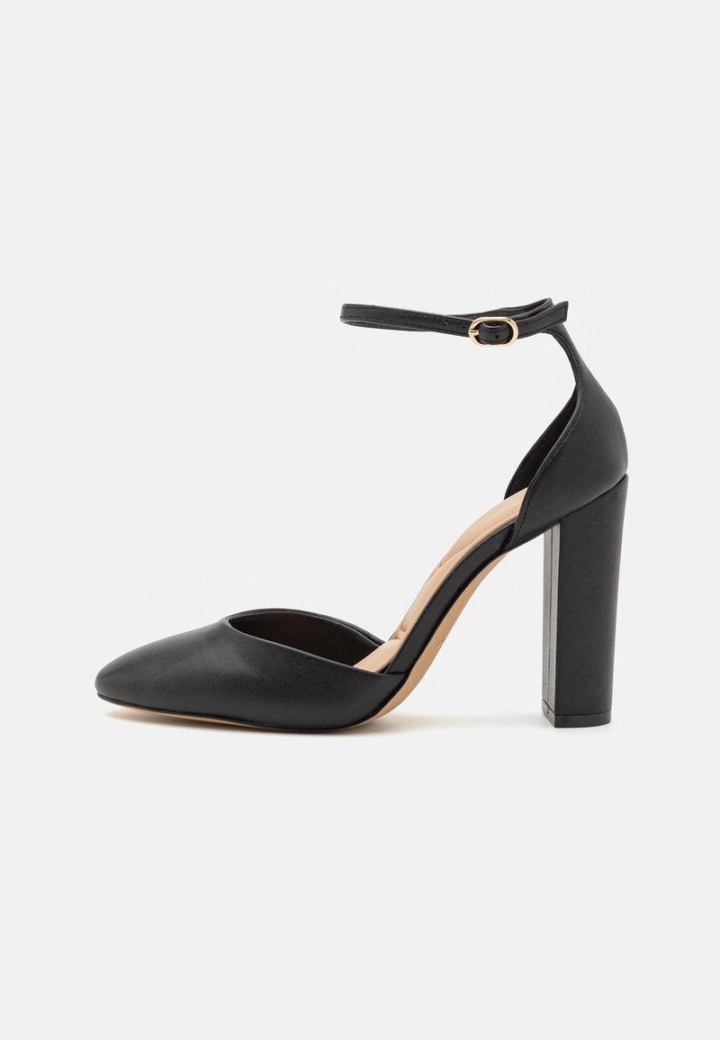 Escarpin noir à talon haut avec une bride de cheville, bout pointu et talon carré. Texture en cuir lisse avec une doublure nude.