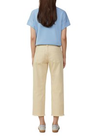 Top corto azzurro chiaro a maniche corte abbinato a jeans a gamba larga color crema, con orli sfrangiati e una vestibilità comoda, completato da scarpe grigie.
