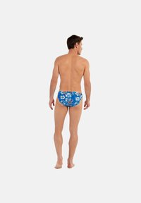 Blaue florale Schwimmunterhosen mit mehrfarbigen tropischen Mustern, mit einem niedrigen Schnitt und einem elastischen Bund, von hinten gesehen.