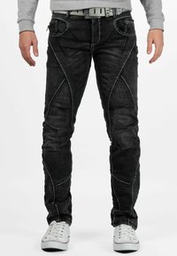 Zwarte denim jeans met contrasterende witte stiknaden, taperende ontwerp, unieke naden en voorzakken. Vergezeld door een grijze sweatshirt en witte sneakers.