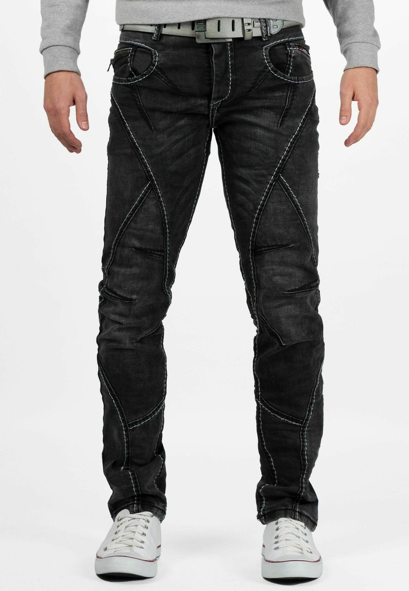 Zwarte denim jeans met contrasterende witte stiknaden, taperende ontwerp, unieke naden en voorzakken. Vergezeld door een grijze sweatshirt en witte sneakers.