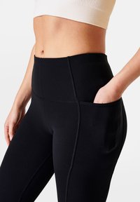 Leggings neri a vita alta realizzati in materiale elasticizzato con cuciture rinforzate e una tasca laterale per il riporre oggetti. Texture liscia e design aderente.