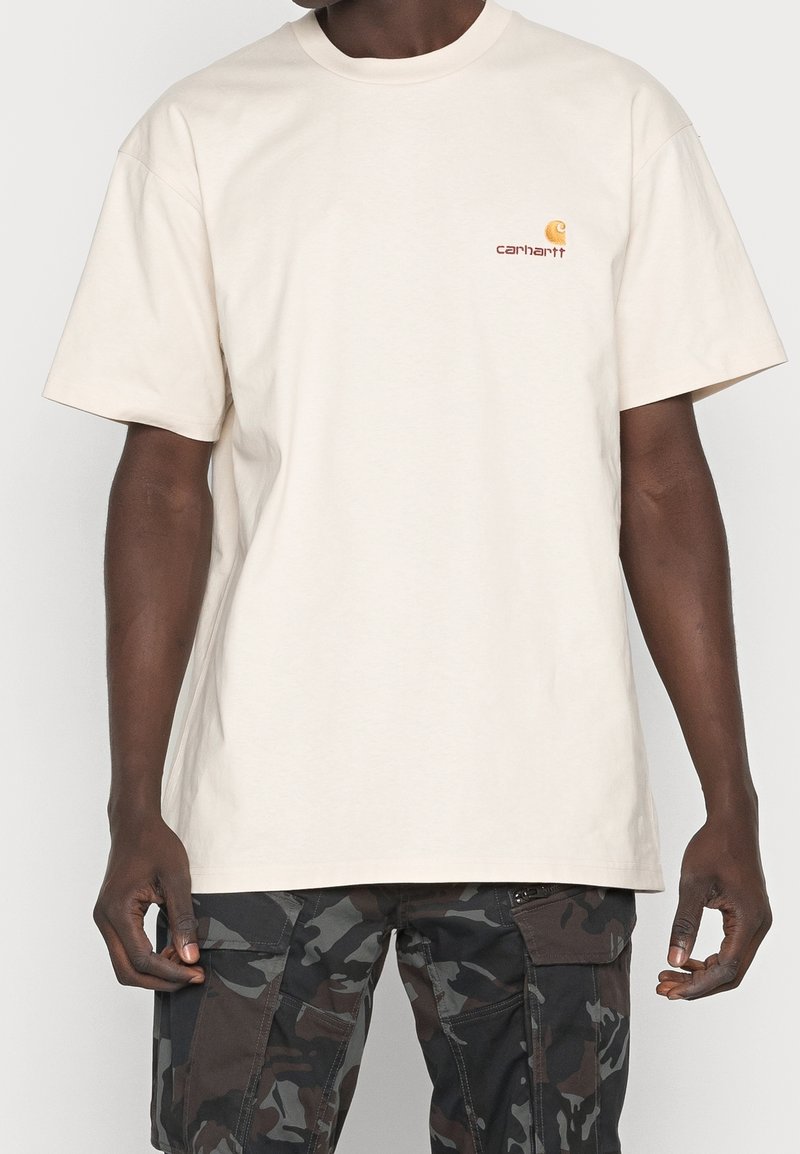 Beige cotton T-shirt featuring a round neckline and short sleeves. Includes a small, orange embroidered logo on the chest.