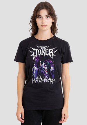 Young woman wearing a black T-shirt featuring a graphic of the Joker character with purple gloves and "The Joker" text above.