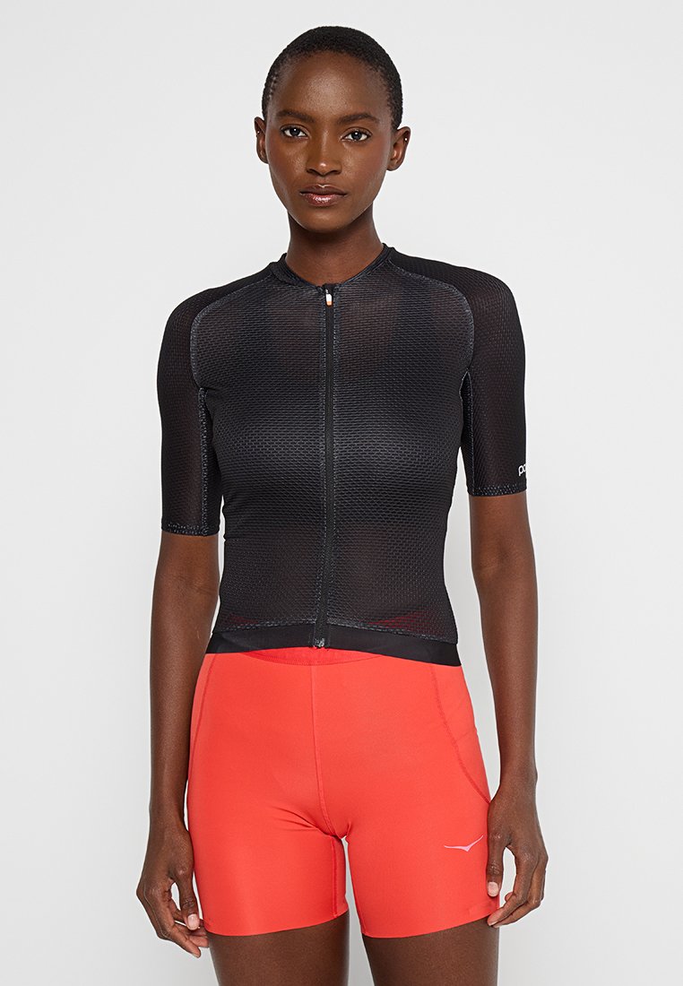 Schwarzes Radtrikot mit kurzen Ärmeln und Mesh-Struktur, Frontreißverschluss und kontrastierenden schwarzen Akzenten, kombiniert mit roten Fahrradhosen.