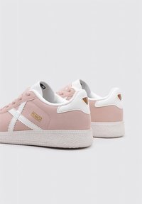Sneakers in suede rosa con accenti bianchi, dotati di una suola testurizzata, lacci tondi e una piccola etichetta marrone sul tallone. Nome del marchio visibile.