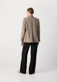 Braun gestreifter Blazer mit einer taillierten Passform, mit Schlitz hinten und vierknöpfigen Manschetten. Kombiniert mit schwarzen, weiten Hosen und beigen Schuhen.