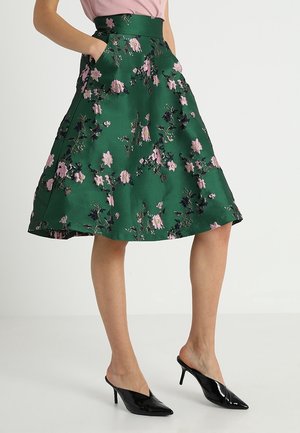 Groene uitlopende rok met roze bloemenborduursel, hoge taille, zijzakken, gecombineerd met zwarte mules met hak en puntige neus.