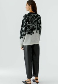 Schwarzer und weißer gestrickter Pullover mit Blumenmuster, grauer Körper, gerippte Bündchen. Kombiniert mit schwarzen, locker sitzenden Lederhosen und flachen Schuhen.