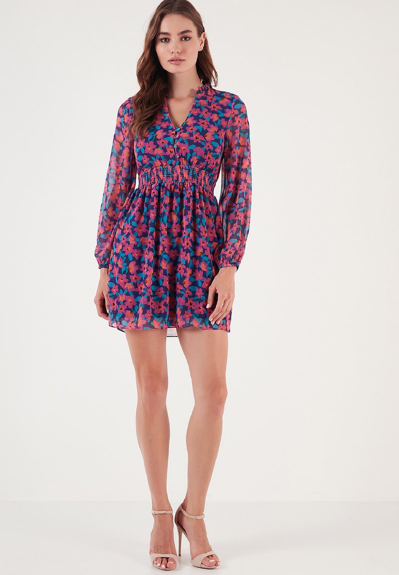 Blumenkleid mit tiefem V-Ausschnitt, transparenten langen Ärmeln, elastischem Bund und Smock-Design. Die Farben umfassen lila, rosa und grün.