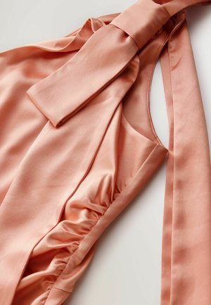 Persiku krāsas satīna topiņš ar sasienamu izgriezuma mezglu, savilktām sānmalām un gludu tekstūru. Aprīkots ar platu, plūstošu mezglu un asimetrisku griezumu.