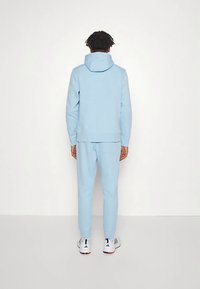 Camisola com capuz azul claro e calças de fato de treino combinando numa mistura de algodão. Apresenta um bolso canguru, punhos canelados e capuz com cordão ajustável.