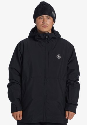 Schwarze wasserdichte Jacke mit Reißverschluss, Kapuze und einem Diamantlogo auf der Brust. Das Design umfasst verstellbare Bündchen und Taschen.