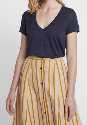 Navy V-neck t-shirt with short sleeves, paired with a beige skirt featuring vertical yellow stripes and black button details down the front.