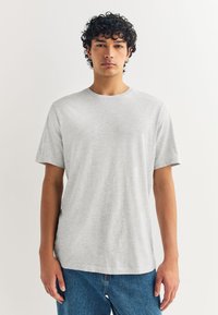 Camiseta de algodón gris con cuello redondo y mangas cortas, con un ajuste holgado y una textura suave, combinada con vaqueros azules.