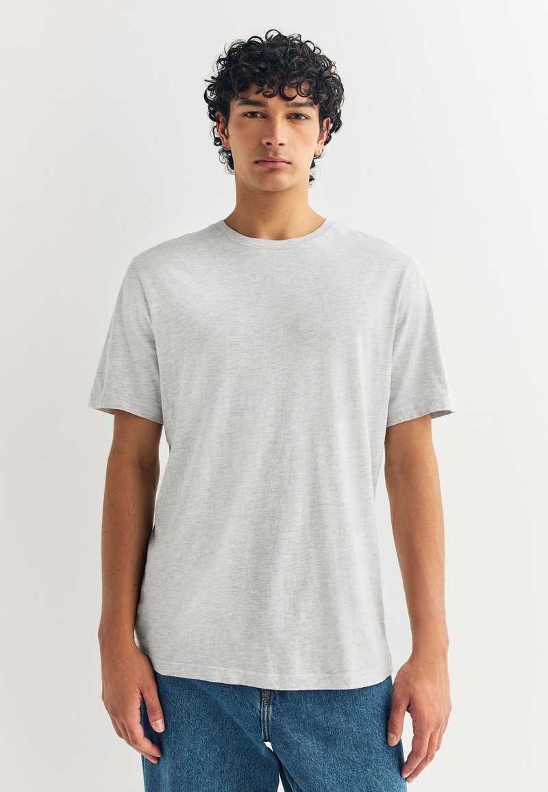 Camiseta de algodón gris con cuello redondo y mangas cortas, con un ajuste holgado y una textura suave, combinada con vaqueros azules.