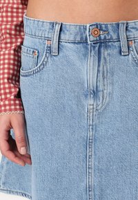 Svetlo modra jeans krila z visokim pasom, vidnimi šivi in sprednjimi žepi. Na pasu je prisotna baker barvna kovinska oprema.