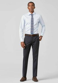 Lichtblauw overhemd, gestreepte stropdas in blauw en bruin, donkere broek, bruine leren riem en bruine suède schoenen.